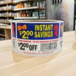 2 dollars off instant savings coupon sticker on a roll of rectangle white labels with red, yellow and blue print