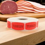 Tuna Salad sticker red identification label with black print on a roll of stickers with sliced turkey in the background